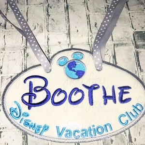 Op de afbeelding: Een witte, ovale deurhanger met blauwe en grijze borduurwerk. De hanger heeft een Mickey Mouse-hoofd met een blauwe wereld in de binnenkant, de tekst "Disney Vacation Club" en de naam "Boothe".