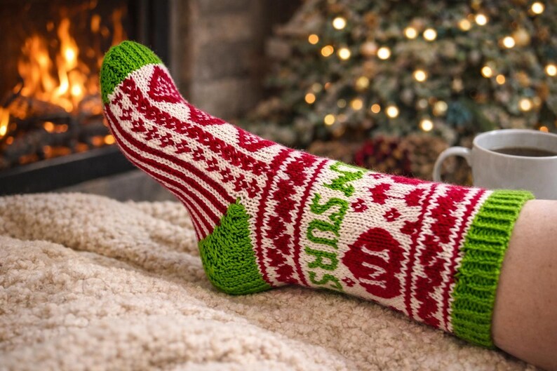 May include: A knitted sock with a festive design, featuring red, white, and green colors. The sock has a patterned design with the word "Mrs" in green. The sock is on a soft, textured surface.