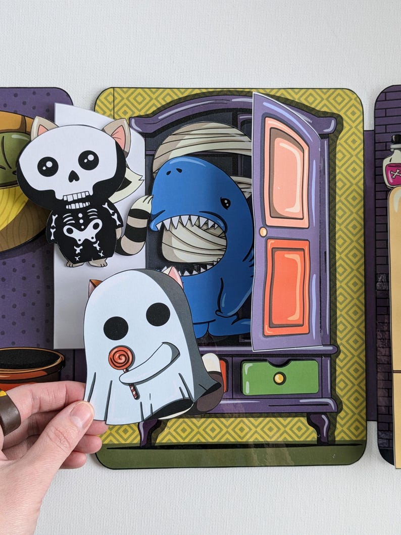 May include: A Halloween-themed children's game with a purple, green, and yellow armoire. The armoire has a door that opens to reveal a blue shark with a white bandage. A ghost with a lollipop is in front of the armoire. A skeleton cat is to the left of the armoire.