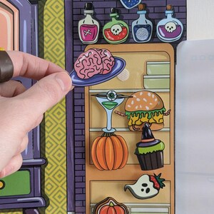 May include: A colorful, illustrated, magnetic refrigerator with a variety of Halloween-themed items, including a brain, a pumpkin, a cupcake, a ghost, a burger, and a martini glass. The refrigerator is open and the items are on the shelves.