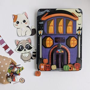 May include: A Halloween-themed playset with a purple house with orange windows and a door that says "Welcome". There are two cut-out figures of a cat and a raccoon, a brown paper bag with candy, and orange pumpkins.
