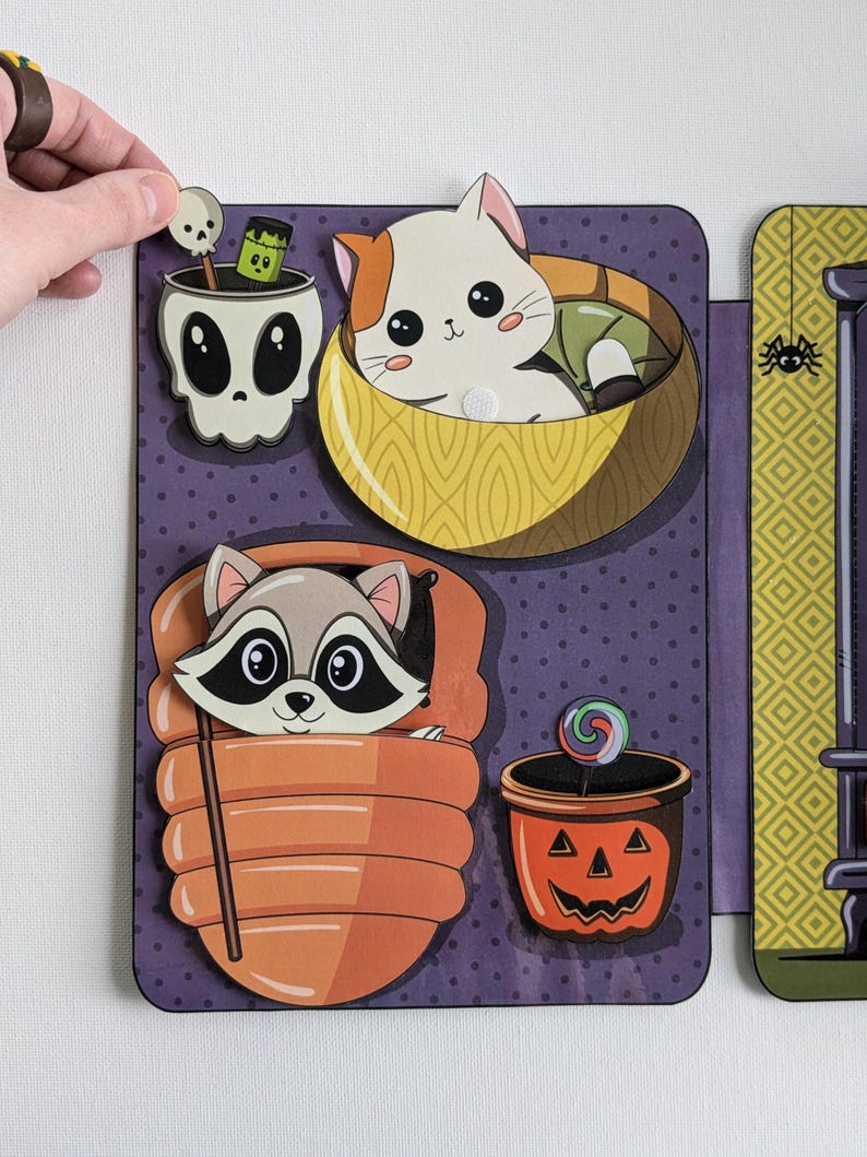 May include: A purple and yellow Halloween-themed felt board with a variety of felt cutouts. The cutouts include a raccoon in a sleeping bag, a cat in a bowl, a skull with a green potion, and a jack-o-lantern with a lollipop.
