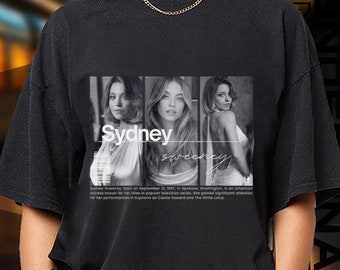 May include: Black t-shirt with a graphic print of three women and the text "Sydney" on the front. The t-shirt is being modeled by a person.