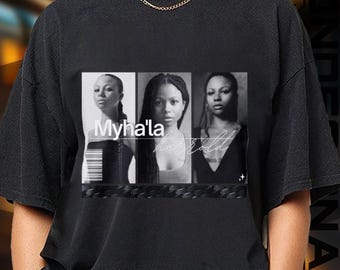 May include: Black t-shirt featuring a grayscale image of three women. The image has the text "Myha'la" and "how bold" in a stylized font. The shirt has a crew neck and short sleeves.