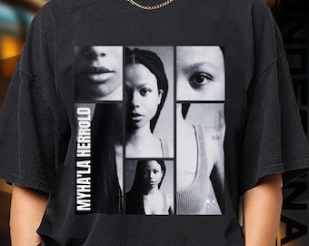 May include: Black t-shirt featuring a collage of black and white images of a person's face and upper body. The text "MYHA'LA HERROLD" is printed vertically on the left side of the shirt. The images are arranged in a grid pattern.