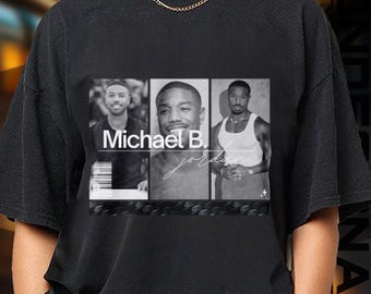 May include: Black t-shirt featuring a graphic of Michael B. Jordan in three different poses. The design includes the text "Michael B. Jordan" in a bold font, with a signature-style script below. The overall design is in black and white.