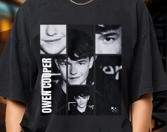 May include: Black t-shirt featuring a collage of black and white images of a person's face. The name "OWEN COOPER" is printed vertically on the left side. The shirt has a crew neck and short sleeves.