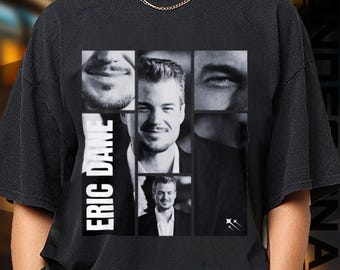May include: Black t-shirt featuring a collage of Eric Dane's face in black and white. The name "ERIC DANE" is printed vertically in white on the left side of the shirt. The design includes various facial close-ups and a full portrait.