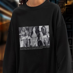 May include: Black sweatshirt with a white graphic print of three women. The text "Sofia Vergara" is printed below the image. The text reads "Sofia Vergara, born on July 10, 1972, in Barranquilla, Colombia, is a Colombian-American actress, model, and TV personality known for her role as Gloria Delgado-Pritchett on Modern Family, earning multiple awards for her role."