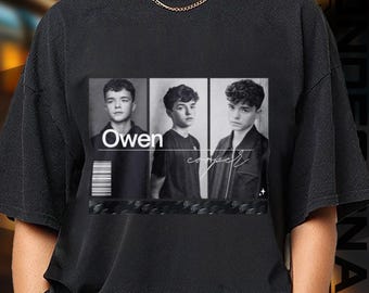 May include: Black t-shirt featuring a black and white image of three young men. The word "Owen" is printed in white, and the name "cooper" is written in cursive. The shirt has a crew neck and short sleeves.