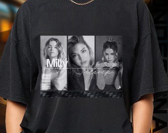 May include: Black t-shirt featuring a black and white graphic of three women. The graphic includes the names "Milky" and "Alcock" in a stylized font. The shirt has a crew neck and short sleeves.