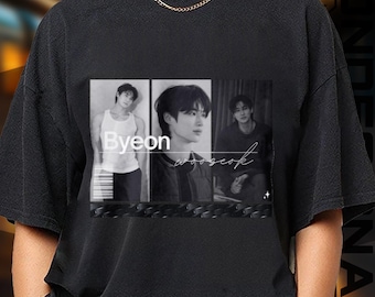 May include: Black t-shirt featuring a grayscale graphic of a person in three different poses. The graphic includes the name "Byeon" and the word "wooseok" in a script font. The shirt has a crew neck and short sleeves.