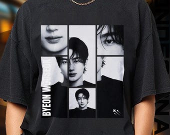 May include: Black t-shirt featuring a collage of black and white images of a person's face. The text "BYEON WOOSEOK" is printed vertically on the left side. The shirt has a crew neck and short sleeves.