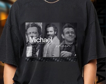 May include: Black t-shirt featuring a black and white image of three men. The image has the name "Michael" in large white letters and the name "sheen" in cursive. The t-shirt is made of a soft material.