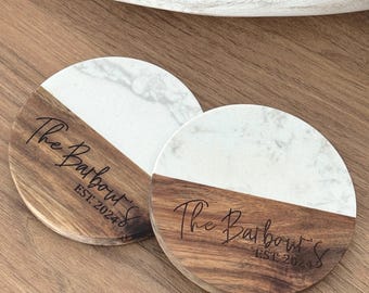 May include: Two round wooden coasters with a white marble top. The coasters are engraved with the text "The Barbour's Est. 2024".