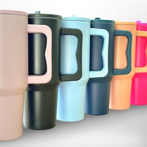 May include: A selection of insulated tumblers in a range of colours: pink, black, light blue, navy, orange, and hot pink. Each tumbler has a matching lid and a large handle. The tumblers are designed to keep drinks cold or hot.