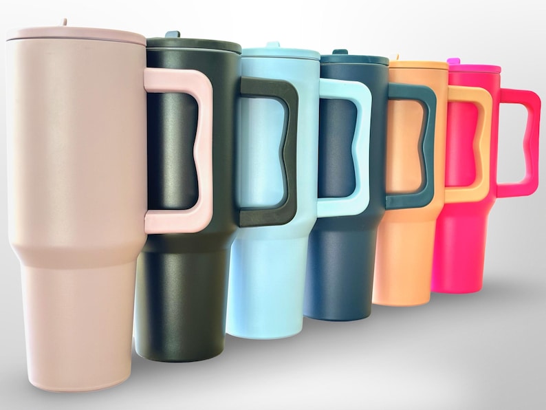 May include: A selection of insulated tumblers in a range of colours: pink, black, light blue, navy, orange, and hot pink. Each tumbler has a matching lid and a large handle. The tumblers are designed to keep drinks cold or hot.