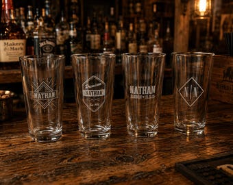 May include: Four clear glass pint glasses arranged in a row, each featuring a unique white etched design. The first glass displays the name Nathan in a diamond frame, the second says Premium Nathan Est. 1986, the third reads Nathan Bestman 01.23.25, and the fourth shows the initials N|N inside a diamond.