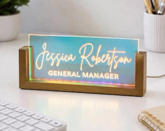 May include: A personalized desk nameplate with the name "Jessica Robertson" and the title "GENERAL MANAGER" in a stylish script font. The nameplate has a wooden base and a glowing, iridescent acrylic panel. A keyboard and office supplies are in the background.