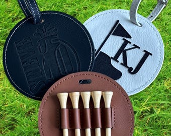 May include: Three round leather luggage tags with a golf theme. One tag is black with a golf cart and the text "FOREVER", another is white with the initials "KJ" and a golf flag, and the third is brown with five golf tees.