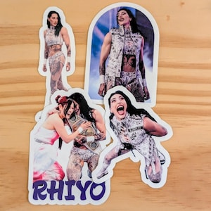 May include: A collection of stickers featuring a female wrestler in various poses. The stickers showcase the wrestler in action, wearing a white and silver outfit with intricate designs and tattoos. One sticker has the word "RHIYO" in purple.