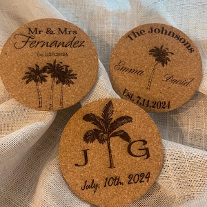 May include: Three round cork coasters with engraved palm trees and text. The first coaster says "Mr & Mrs Fernandez Est. 5.20.2024". The second coaster says "The Johnsons Emma David Est. 7.14.2024". The third coaster says "J G July, 10th, 2024".