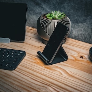 May include: A black smartphone stand with a phone in it, a black keyboard, a gray laptop stand, a gray planter with a succulent plant, and a black and white marble dish on a wooden table.