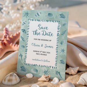 May include: A teal "Save the Date" card with seashell illustrations, featuring text for Olivia & James' wedding in Nice, France. The card is surrounded by seashells, a starfish, and coral on a sandy beach.