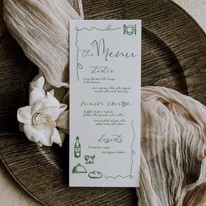 May include: A white menu card with green text and illustrations, featuring a handwritten style. The menu includes starters, main courses, and desserts. The card is placed on a wooden charger with a white flower and draped fabric.
