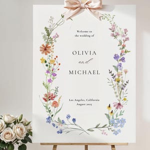 May include: A white wedding welcome sign with a floral wreath border. The sign reads "Welcome to the wedding of Olivia and Michael, Los Angeles, California, August 2023".