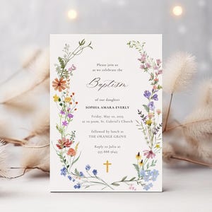 Op de afbeelding: Een bloemige doop uitnodiging met een witte achtergrond en een krans van kleurrijke wilde bloemen. De tekst luidt: "U bent van harte welkom om samen met ons de doop van onze dochter Sophia Amara Everly te vieren, op vrijdag 10 mei 2015 om 10:00 uur in de St. Gabriel's Church, gevolgd door een lunch in The Orange Grove. Reageer naar Julia op 555 888 5643."