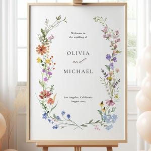 May include: A wedding sign with a floral wreath design. The sign says "Welcome to the wedding of Olivia and Michael, Los Angeles, California, August 2025".