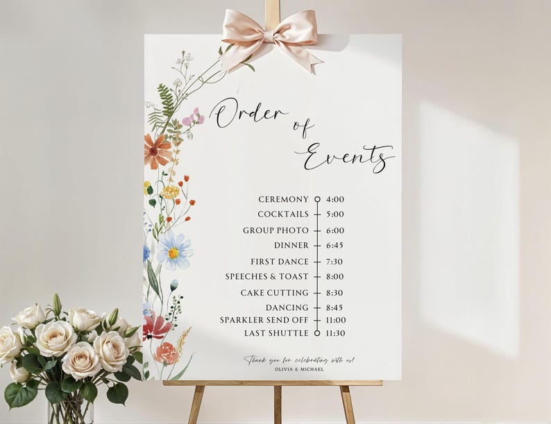 May include: A white wedding sign with a floral border and a list of events with corresponding times. The sign reads "Order of Events" and includes events such as "Ceremony", "Cocktails", "Group Photo", "Dinner", "First Dance", "Speeches & Toast", "Cake Cutting", "Dancing", "Sparkler Send Off", and "Last Shuttle".