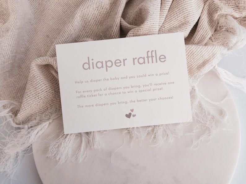 May include: A white card with the text "diaper raffle" in pink lettering. The card has instructions for a diaper raffle, encouraging guests to bring diapers for a chance to win a prize. The text reads: "Help us diaper the baby and you could win a prize! For every pack of diapers you bring, you'll receive one raffle ticket for a chance to win a special prize! The more diapers you bring, the better your chances!"