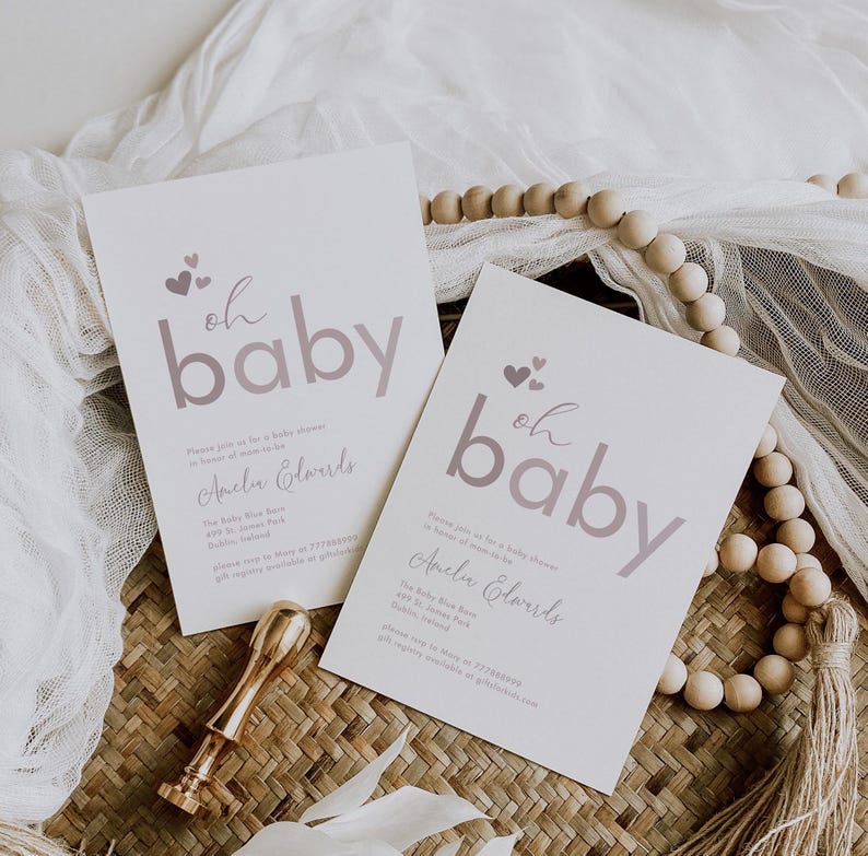 May include: Two white baby shower invitations with a pink and white "oh baby" design. The invitations feature a pink heart design and the text "Amelia Edwards".
