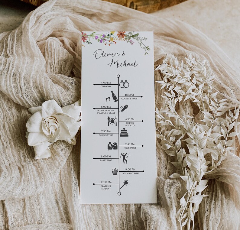 May include: A white wedding timeline card with floral accents and the names "Olivia & Michael" in elegant script. The card details the wedding schedule with icons representing each event, such as the ceremony, cocktail hour, and first dance.