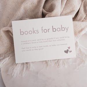 May include: A white card with the text "books for baby" in pink lettering. The card has a message asking guests to bring a children's book instead of a card for the baby. The card is decorated with pink hearts.