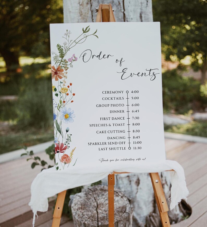 May include: A white sign with a floral design on the left side and a list of wedding events with times on the right side. The sign reads "Order of Events" and lists the following events: Ceremony, Cocktails, Group Photo, Dinner, First Dance, Speeches & Toast, Cake Cutting, Dancing, Sparkler Send Off, Last Shuttle. The sign also includes the times for each event.