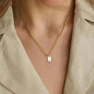 May include: A gold chain necklace with a small rectangular pendant featuring the letter 'A'.