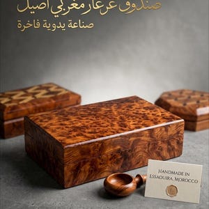 Peut inclure: Une boîte rectangulaire en bois avec un grain de bois loupe poli et tourbillonnant. À côté se trouvent une petite cuillère en bois et une carte crème avec le texte "HANDMADE IN ESSAOUIRA, MOROCCO" et un sceau doré. Deux autres boîtes sont visibles.