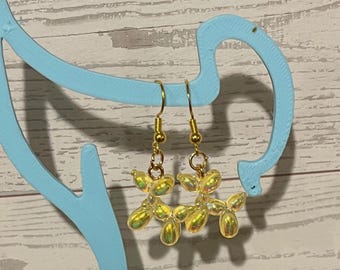 Könnte beinhalten: Ein Paar Ohrhänger mit irisierenden gelben Luftballonhund-Anhängern, die an goldfarbenen Metallhaken hängen. Die Anhänger haben eine glänzende, reflektierende Oberfläche, die das Licht einfängt und einen schillernden Glanz erzeugt.