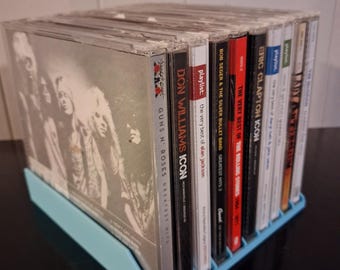Könnte beinhalten: Ein hellblaues Kunststoff-Aufbewahrungsregal mit einer Reihe von Musik-CDs. Die Sammlung umfasst Alben von Guns N' Roses, Don Williams, Alan Jackson, Bob Seger, The Rolling Stones, Eric Clapton, Daryl Hall und John Oates sowie Lady Antebellum.