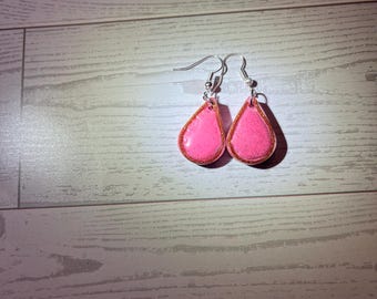 Könnte beinhalten: Ein Paar tropfenförmige Ohrringe mit einer leuchtend rosa Mitte und einem dezenten Glitzer-Finish. Jeder Ohrring ist von einem dünnen, kupferfarbenen Metallrand umgeben und hängt an einem silberfarbenen Metallhaken für durchstochene Ohren.