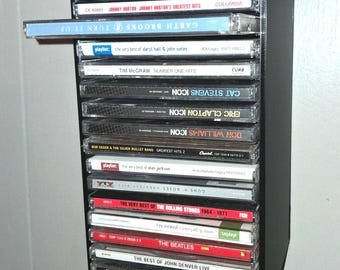 Könnte beinhalten: Ein schwarzes Wandregal zur CD-Aufbewahrung mit einem vertikalen Stapel von Musikalben. Eine CD-Hülle ist teilweise aus dem Regal herausgezogen. Die Sammlung enthält Titel von Garth Brooks, Lady Antebellum, Johnny Horton und The Beatles.