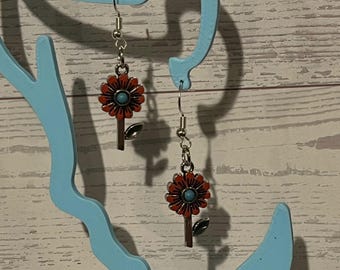 Könnte beinhalten: Ein Paar Ohrhänger mit einem silberfarbenen Metallblumenmotiv, orangefarbenen Blütenblättern und einer kleinen türkisfarbenen Perle in der Mitte. Jeder Ohrring hängt an einem silberfarbenen Haken und hat ein einzelnes grünes Blatt am Stiel.