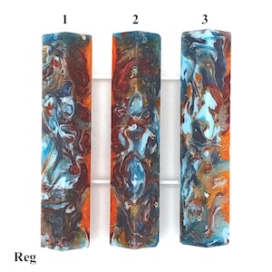 May include: Three rectangular resin pen blanks labeled 1, 2, and 3, featuring a marbled pattern of bright orange, sky blue, deep brown, and metallic gold swirls. The word Reg is printed in the bottom left corner of the image.