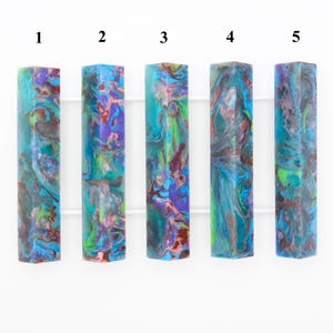 Puede incluir: Cinco diferentes blancos de resina de colores con un patrón de mármol en tonos de azul, verde, morado y marrón. Los blancos están numerados del 1 al 5.