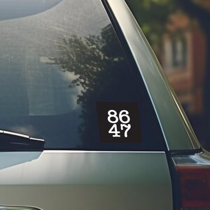 Puede incluir: Una pegatina cuadrada negra con los n&uacute;meros blancos 86 y 47 en la ventana de un coche plateado.