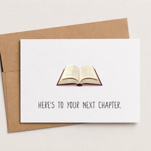 May include: A white greeting card with a brown kraft envelope featuring an illustration of an open book with cream pages and a dark red cover, accompanied by the black text that reads, HERE'S TO YOUR NEXT CHAPTER, centered below the book.