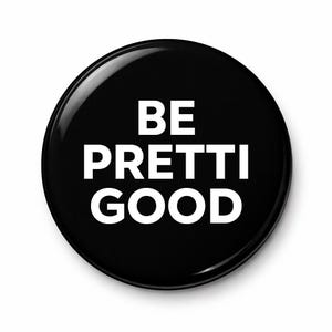 May include: A glossy black button with the words "BE PRETTI GOOD" in bold white capital letters. The button is round and has a reflective surface, with a slight sheen.